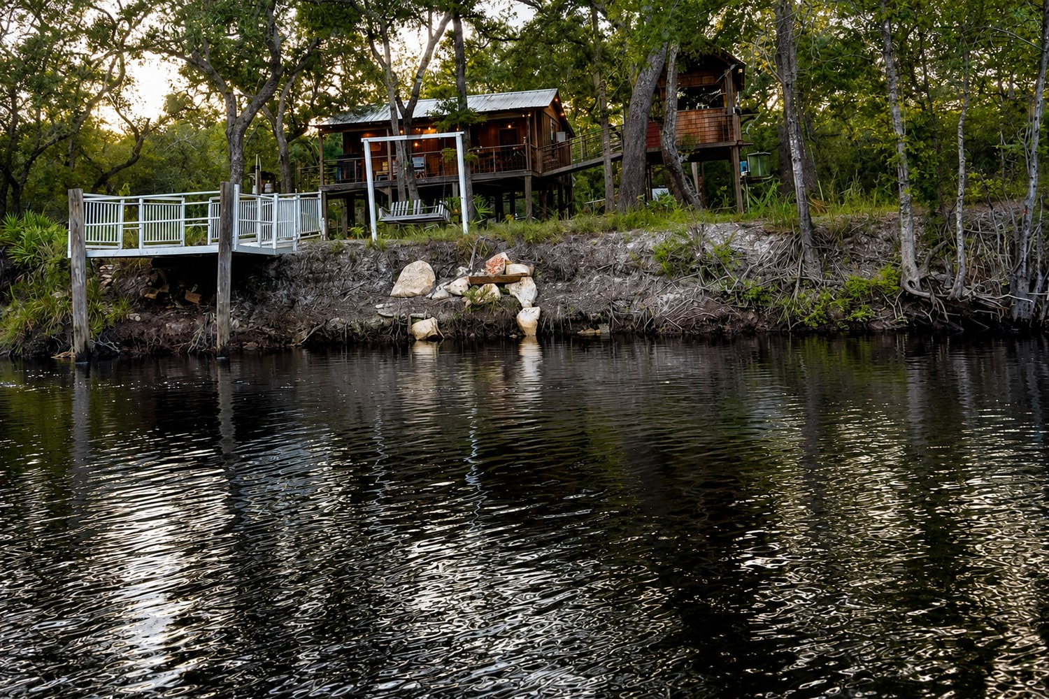 Two riverfront cabins on stilts above the St. Marys River near the Okefenokee Swamp in Folkston, Georgia, with a private white railed dock at the water
