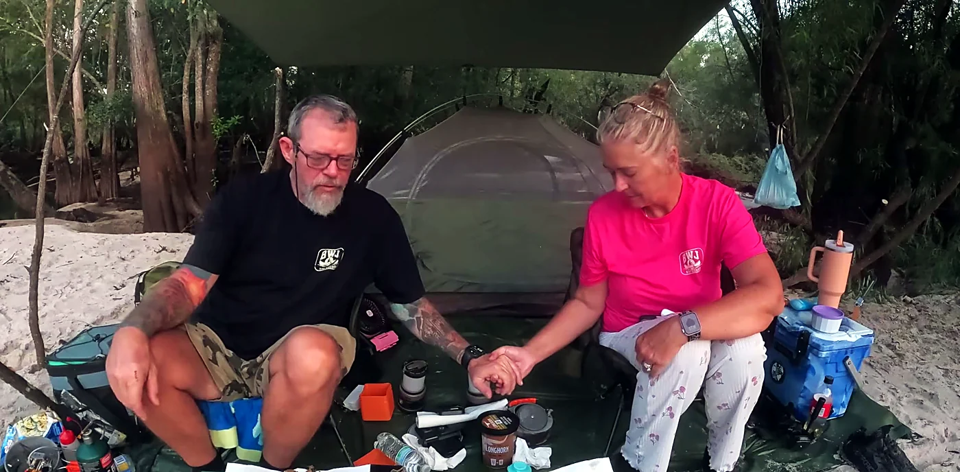 Rodney and Tina holding hands to say the blessing over a supper of fried fish, under a tarp beside their tent on a Satilla River sandbar